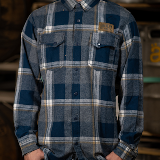 Blue and grey plaid flannel shirt with leather Bravery Brewing logo patch above left chest pocket
