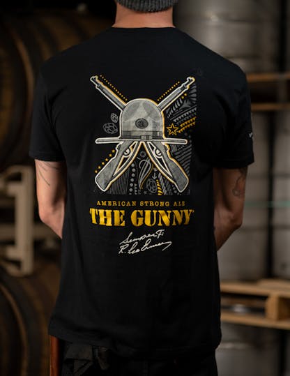 Back of black t-shirt with white and yellow gun and hat design, yellow text below reads, "The Gunny"