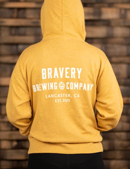 Yellow zip-up hoodie with large white text on the back reading, "Bravery Brewing Company, Lancaster CA, est. 2011"