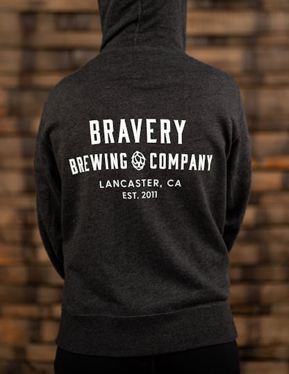 Grey zip-up hoodie with large white text on the back reading, "Bravery Brewing Company, Lancaster CA, est. 2011"