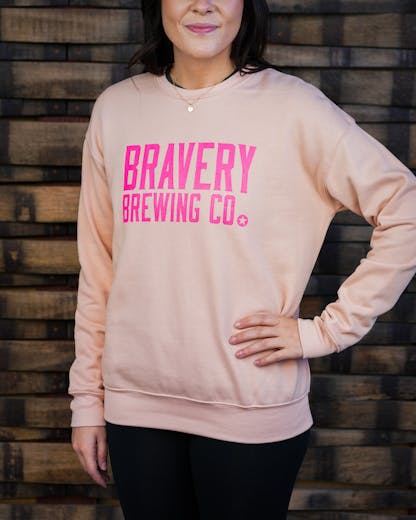 Woman in light pink sweatshirt, "Bravery Brewing" in hot pink lettering