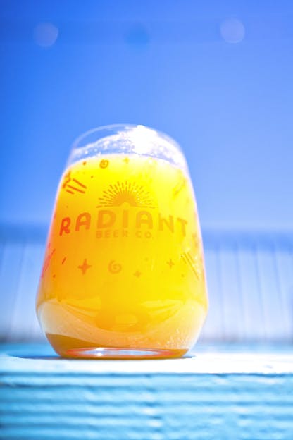 Bright beer in a Radiant Beer Co logo glass in the sun