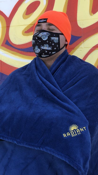 Person wrapped in cozy navy blue blanket with Radiant Beer Co. logo