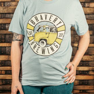 front of light blue t-shirt with a circular design with the text "Bravery Brewing, Est. 2011." In the center of the circle is an illustrated vintage style van with a basset hound sticking it's head out of the car window. The dogs ears are drawn to be flowing in the wind.
