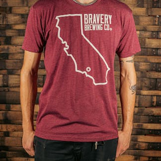 front of a red heather t-shirt. There is a large outline of the state of California with a star near the bottom of the state where Bravery is located. Next to the outline of the state is the text "Bravery Brewing Co." Both the illustration and text are printed in white ink.
