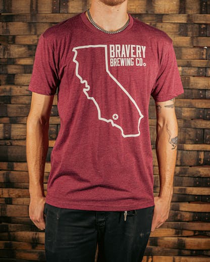 front of a red heather t-shirt. There is a large outline of the state of California with a star near the bottom of the state where Bravery is located. Next to the outline of the state is the text "Bravery Brewing Co." Both the illustration and text are printed in white ink.