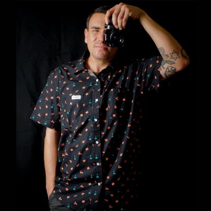 man holding camera up to face in an all over pattern button up shirt