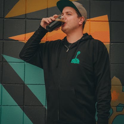 man drinking a beer in a black zip up hoodie