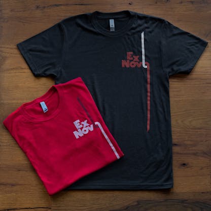 two shirts on wood floor, red folded in a square partially atop graphite black, both have contrast color logos with lines, text "Ex Novo"