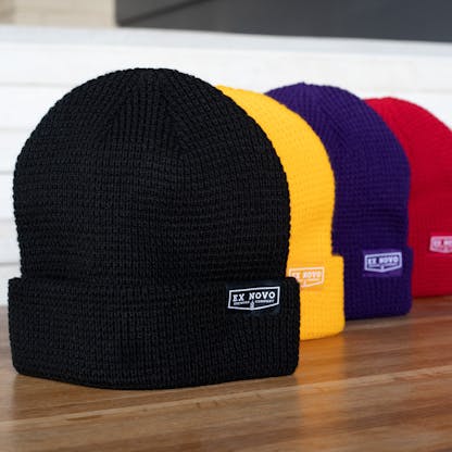 four waffle knit beanies lined up black, yellow, purple, then red in back each with clip tag text "Ex Novo Brewing Company"