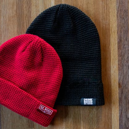 red waffle knit beanie on top of black waffle knit beanie each with clip tags with text "Ex Novo Brewing Company" and "Drink Beer Do Good"
