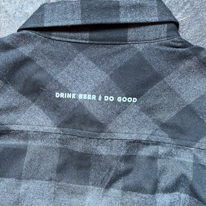 close up of back collar and shoulders of black and charcoal flannel shirt with small white print "Drink Beer Do Good"