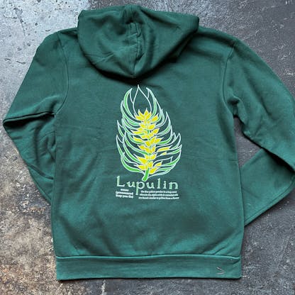 green hoodie on a concrete floor, back view with arms folded beneath, on back is visible yellow and light green illustration of a hop cone with description beneath, text "Lupulin noun: (pronounced loop-you-lin) the fine yellow powder in a hop cone wherein the alpha acids & essential oils are found; similar to pollen from a flower"