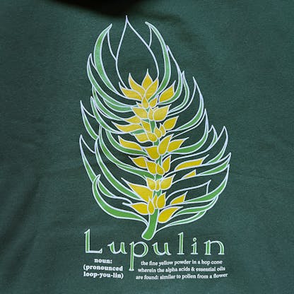 close up of green shirt with yellow and light green illustration of a hop cone with description beneath, text "Lupulin noun: (pronounced loop-you-lin) the fine yellow powder in a hop cone wherein the alpha acids & essential oils are found; similar to pollen from a flower"