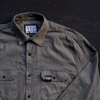 partial view of greyish sage green long sleeve button up collared shirt with small custom left chest pocket black clip tag and internal custom black and white tag text "Drink Beer Do Good"