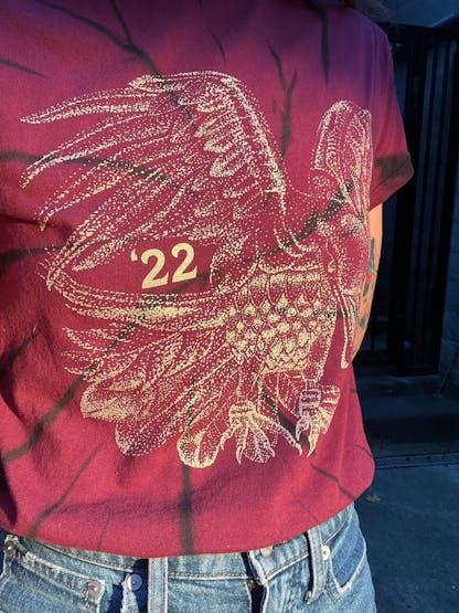 close shot of a person's torso wearing a maroon shirt with black tie dye swirls and shiny gold print of a large raven design and number '22