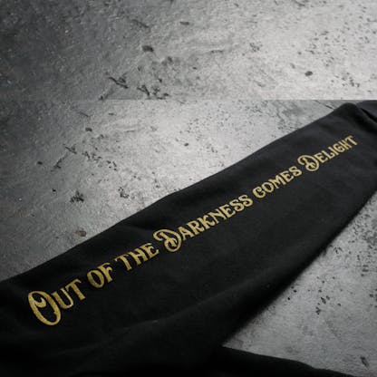 extended sleeve of black sweatshirt with gold lettering text "Out of the Darkness Comes Delight"