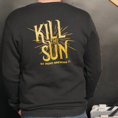 back view of person wearing a black crewneck sweatshirt with bright gold logo text "Kill The Sun" and smaller text beneath "Ex Novo Brewing Co."