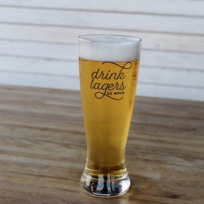 tall curved pint glass with heavy belled glass base features black cursive text "drink lagers" and small block text "Ex Novo"