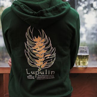 cropped torso view of person wearing green hooded sweatshirt with large green and yellow stylized hop cone illustration text "Lupulin" and smaller unreadable descriptive text