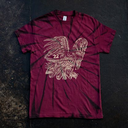 maroon and black swirl dyed shirt on concrete floor with large gold print raven illustration and small text "'22"