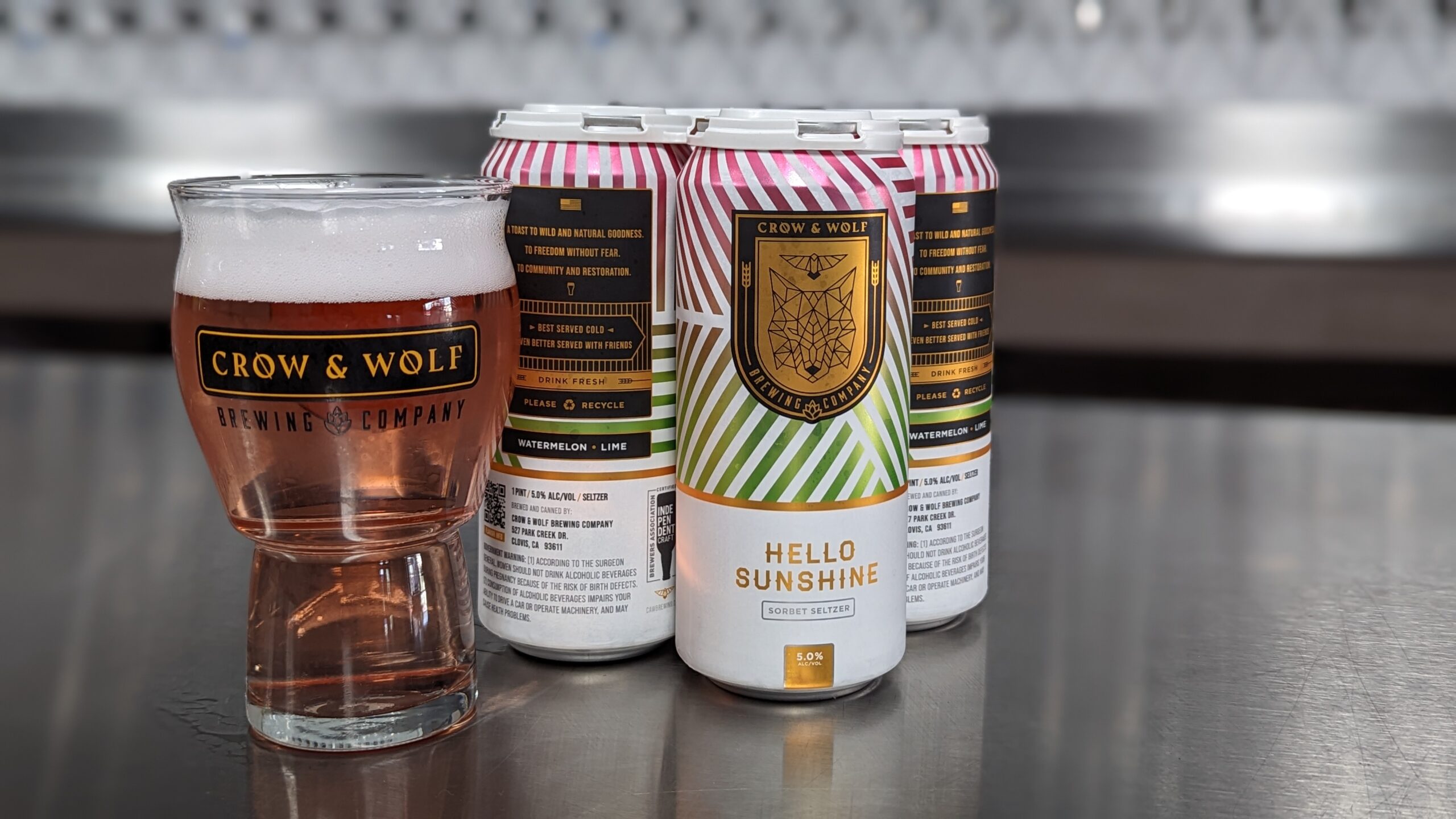 Hello Sunshine watermelon lime seltzer 4-pack of cans and filled Craft Master Grand glass with tap handles in background