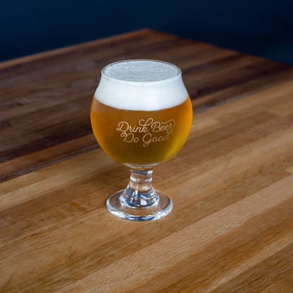 small goblet glass filled with gold beer with white foam head and gold cursive text "Drink Beer Do Good"