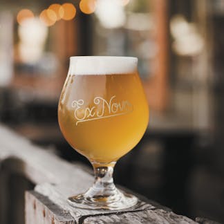 Glass goblet filled with beer and cream colored Ex Novo in cursive font centered on the goblet