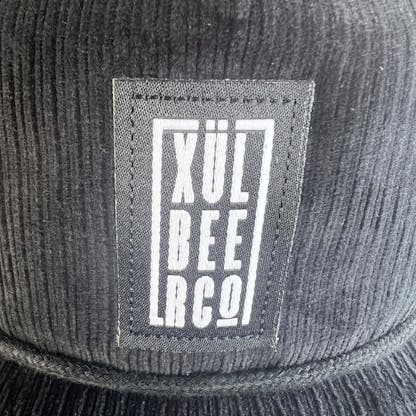 black patch with white xul beer co logo on black corduroy hat