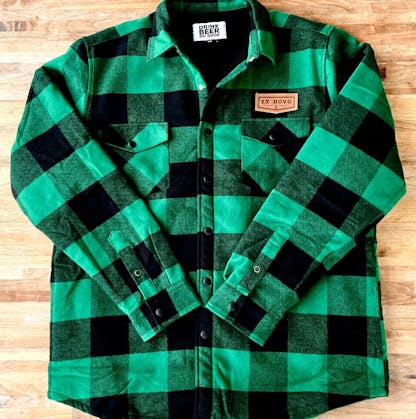 green and black plaid jacket with black snap closures laid out on table, faux leather chest patch text "Ex Novo" in chevron logo, interior custom white tag with black text "Drink Beer Do Good"