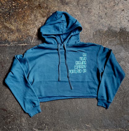 turquoise cropped pullover hooded sweatshirt lays flat on concrete floor, front chest features stacked text "Ex Novo Brewng Company Portland - OR"