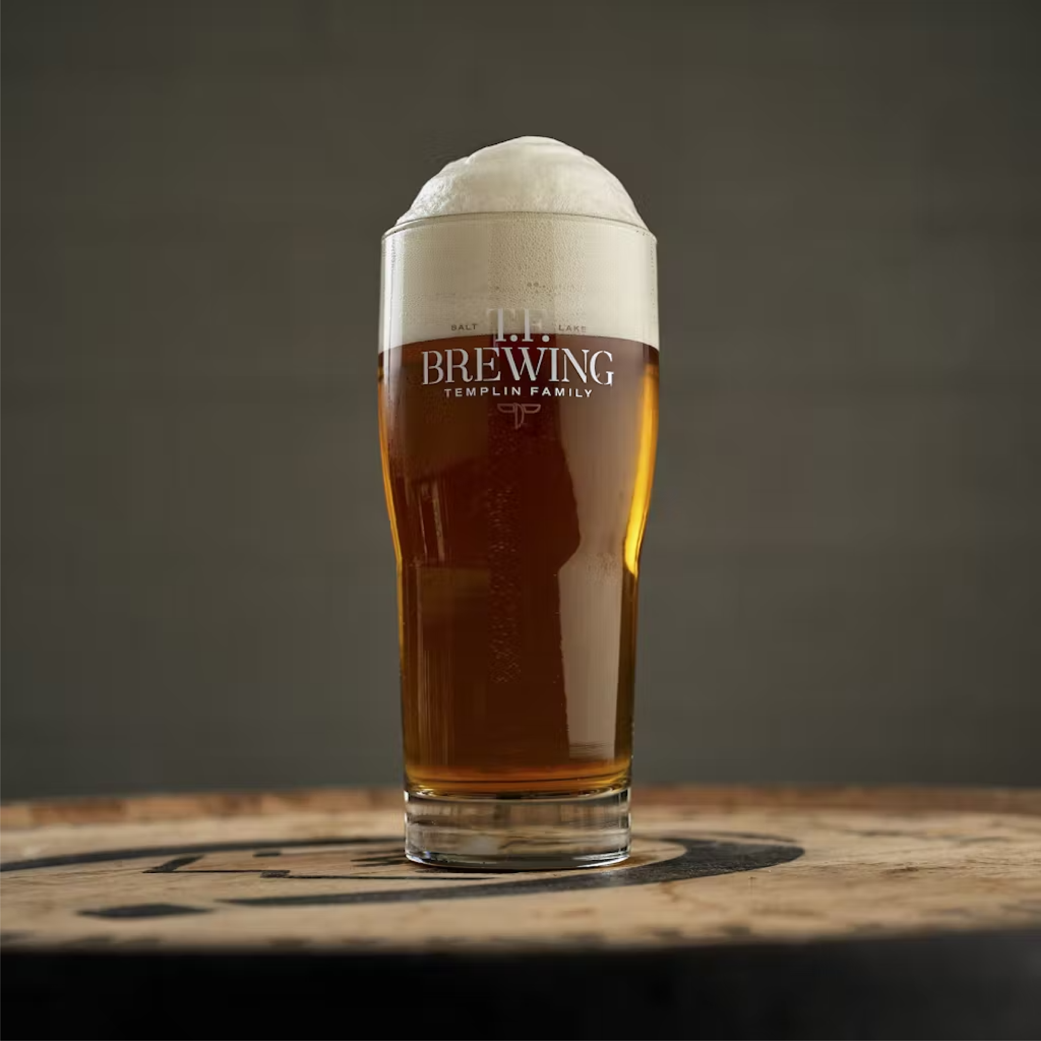 Traditional ale glass filled with burnt honey colored beer sitting on top of a barrel.