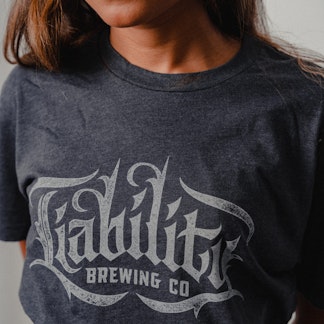 woman wearing charcoal shirt with Liability Brewing