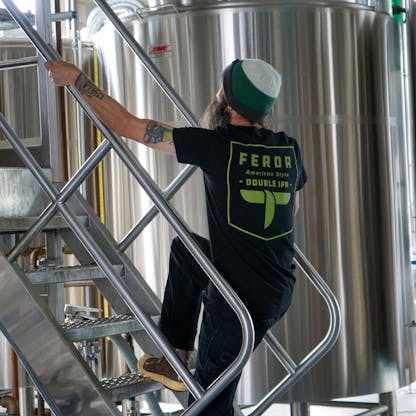 Male walking up stairs to the brew deck wearing a black t-shirt with "ferda american style double IPA" in green print. Just doing brewer stuff.
