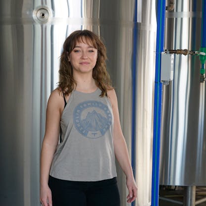 female wearing high neck cut tank in gray with a Templin Family Brewing logo placed around a mountain on center of shirt.