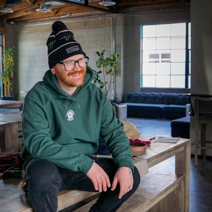 Male wearing Aspen green hoodie with white embroidered T.F. logo on upper center chest sitting on a table in a taproom.
