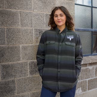 Female wearing a padded outdoor jacket with embroidered T.F. logo on upper left chest.