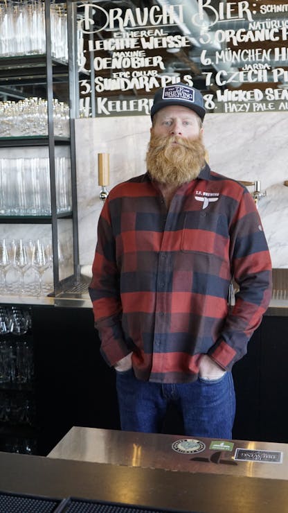 Male wearing black and red block pattern long sleeve with embroidered T.F. logo on upper left chest standing in a taproom.