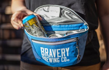 Bravery brewing Fanny Pack Cooler blue, photo has a hand pulling a can of Köbi out of the fanny pack.