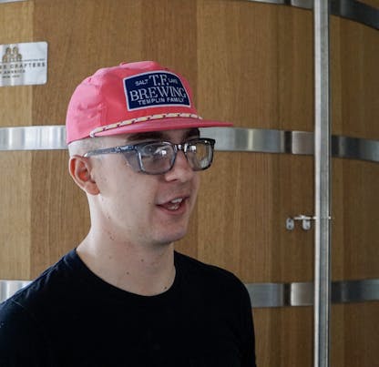 Male in safety goggles wearing a very pink hat with a NAVY TF Brewing logo patch with white writing on center of hat.