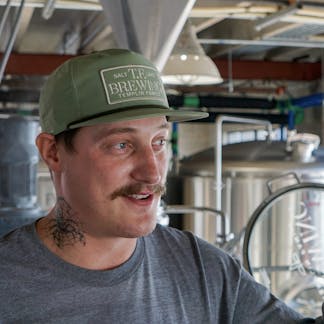 Male wearing a sage green hat with a TF Brewing logo patch in the same color.