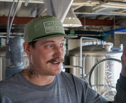 Male wearing a sage green hat with a TF Brewing logo patch in the same color.