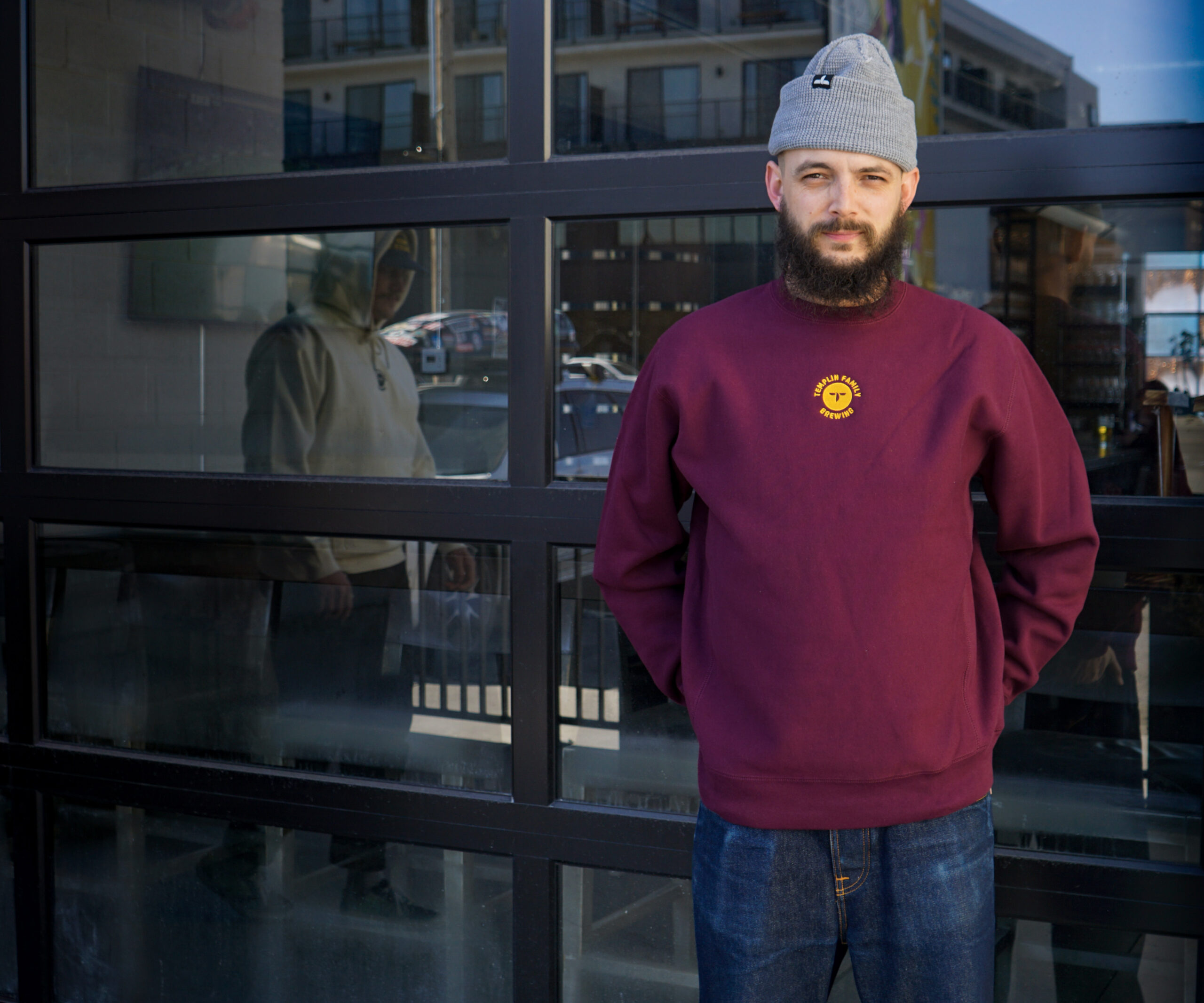 A guy wearing a maroon crew sweatshirt with a gold logo center chest, available to purchase on our website, at $75 plus tax.