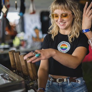 Female wearing a T.F. rainbow logo black shirt pouring beer at a beer festival.