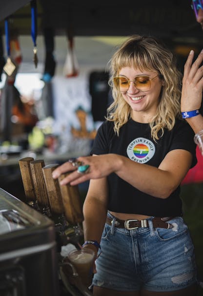 Female wearing a T.F. rainbow logo black shirt pouring beer at a beer festival.