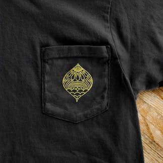 close up view of front chest pocket of black cotton t-shirt with gold line art in tear drop shape