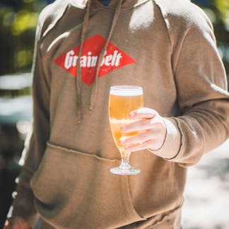 A man wearing a sweatshirt holding a glass of beer outside 