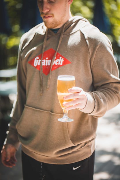 A man wearing a sweatshirt holding a glass of beer outside 