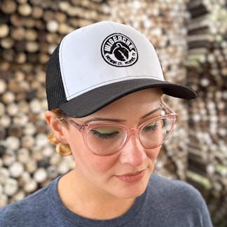 a person modeling a mesh trucker hat with a black bill, white front panel with the wiseacre logo embroidered on it, and black mesh