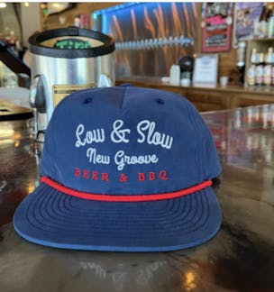 A and red hat sitting on the bar that says low and SLOW New groove beer and bbq